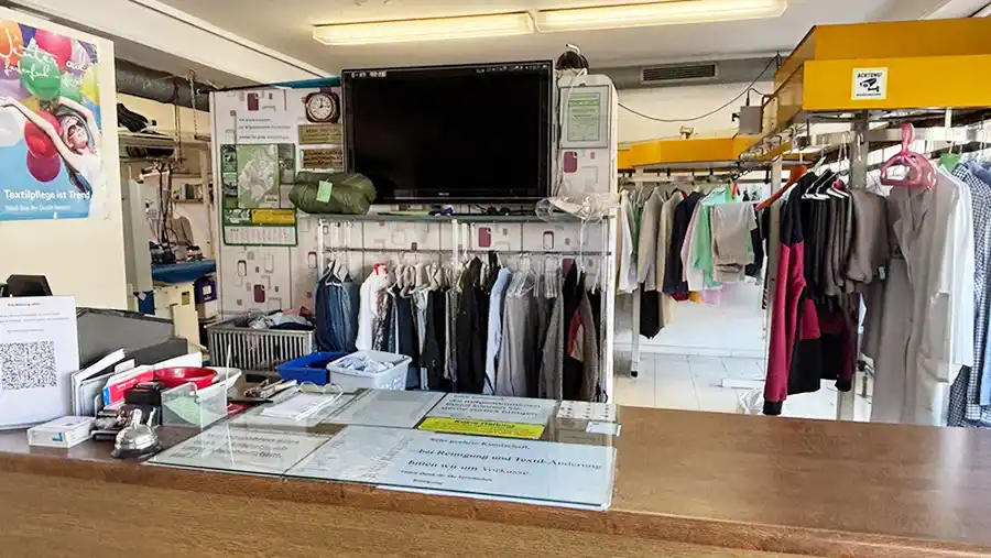 Blick auf eine Theke, im Hintergrund hängen gereinigte Textilien auf Bügeln